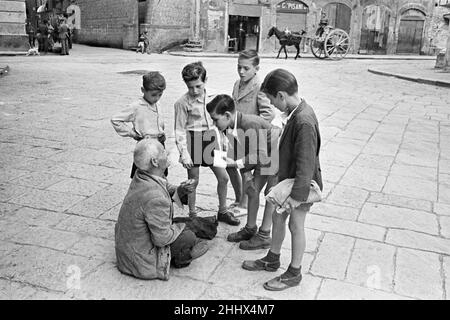 Scenes in Naples, southern Italy showing young boys talk to a beggar in the city streets.Circa 1955. Stock Photo