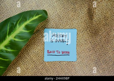 Holiday is Over! - Back To Work write on sticky notes isolated on Wooden Table. Stock Photo