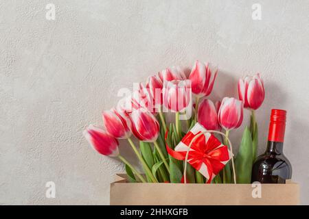 Mother's Day or Women's Day, birthday, wedding congratulation. Spring tulips with a gift box and a bottle of wine in a paper bag. Stock Photo