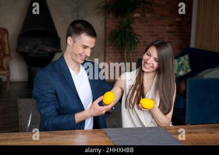 Romantic mature couple enjoying at home after office. Cheerful man and beautiful woman are hugging and giving each other a lemon fruit. Handsome man and woman spend evening together at home happy. Stock Photo