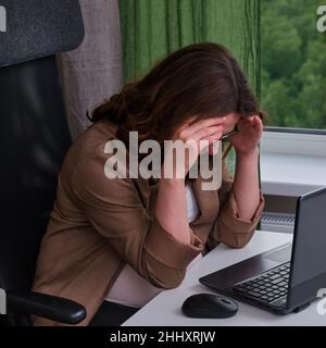 Pregnant woman with laptop in home office crying holding her head Stock Photo