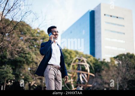 Business black man walking down the street while using his smartphone Stock Photo
