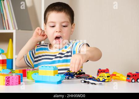 A handsome boy of 4 years old plays with cars and a construction set, games of preschool children, development of imagination. Stock Photo