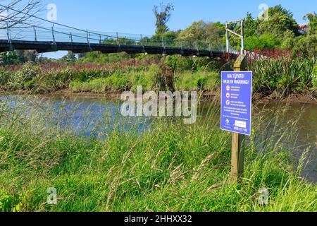 A sign warning of water pollution beside a stream in Tauranga, New Zealand. The bilingual sign is written in English and Maori Stock Photo