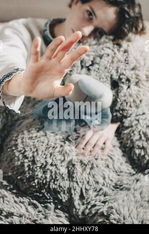 teenage girl in ethnic white embroidered shirt, with chestnut curly hair, sits hugging teddy bear, putting hand forward. concept no to domestic violen Stock Photo