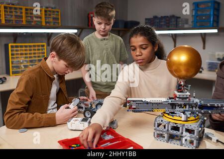Group of children building robots in team while sitting at the table at robotics school Stock Photo