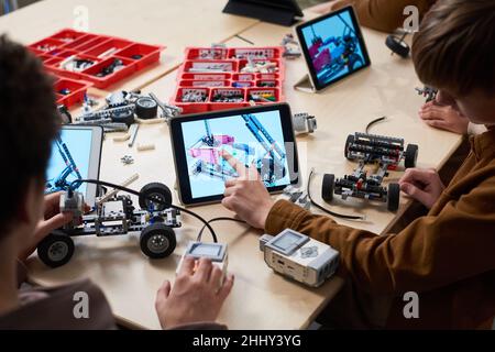 Rear view of boy touching the screen of digital tablet he controlling his robot with computer while sitting at the table at robotics lesson Stock Photo