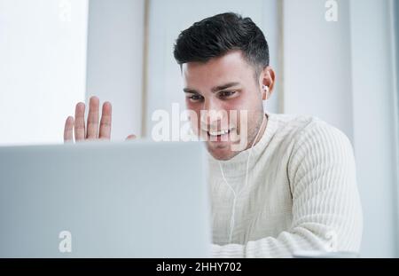 Hope everyone is doing well. Shot of a young man using a laptop to make a video call while working from home. Stock Photo