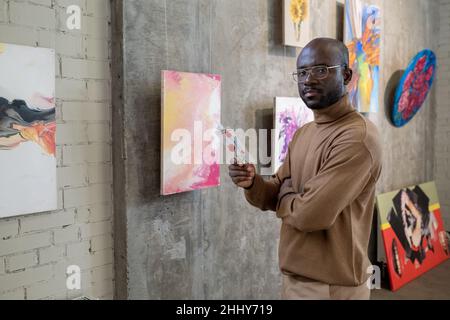 Portrait of African young man looking at camera while reading a brochure in art gallery Stock Photo
