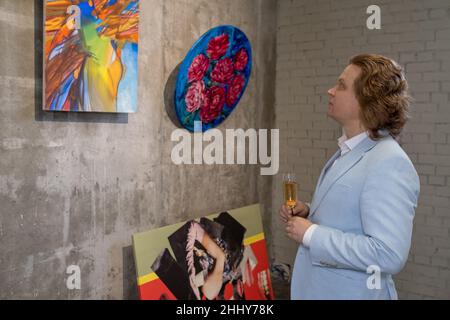 Mature man in suit drinking champagne and looking at paintings with pensive sight at art gallery Stock Photo