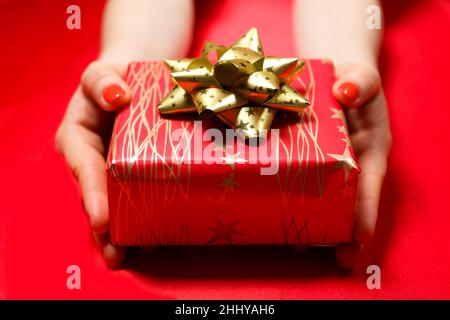 Red beautiful gift with yellow golden bow in the hands of a woman with red nail polish. Stock Photo