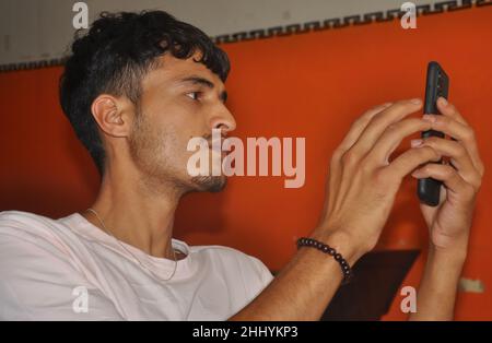 Closeup side view of a young guy using his phone while sitting indoors Stock Photo