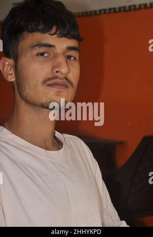Closeup of a handsome Indian young guy sitting indoors with looking at camera Stock Photo