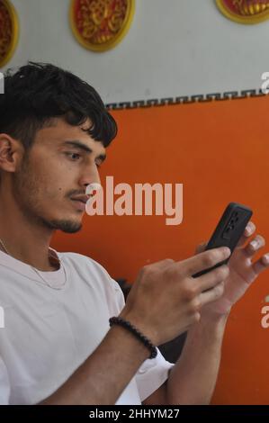 Side view of a good looking young men using phone while sitting indoors Stock Photo