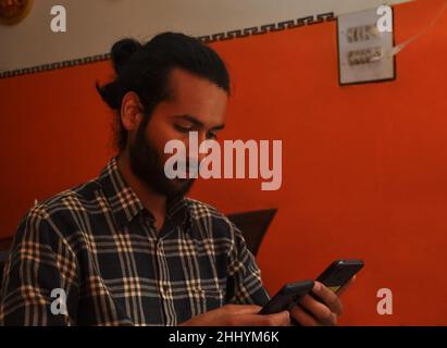 Close-up side view of a handsome bearded man with hair bun, holding two phones - Stock Photo Stock Photo