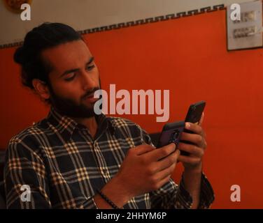 Close-up side view of a handsome bearded man with hair bun, holding two phones - Stock Photo Stock Photo