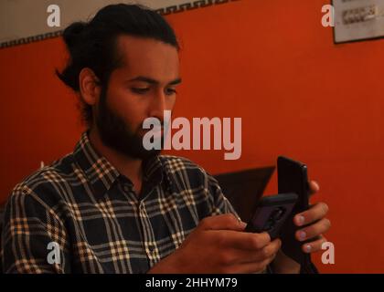 Close-up side view of a handsome bearded man with hair bun, holding two phones - Stock Photo Stock Photo