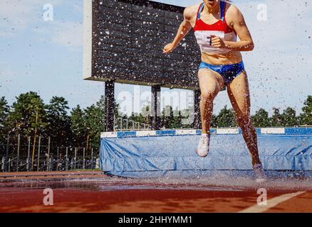 female athlete running steeplechase in athletics competition Stock Photo