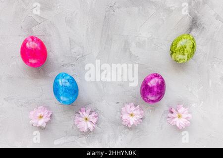 Colorful eggs and spring pink sakura cherry blossom flowers on gray background. Easter celebration concept. Top view, flat lay, copy space Stock Photo