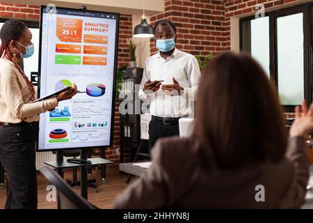African american entrepreneurs showing management presentation explaining business graphs working at company partnership in startup office. Businessteam with medical face mask against covid19 Stock Photo