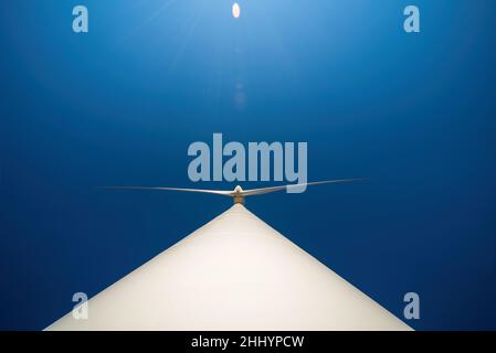 Large three-bladed horizontal-axis wind turbine against clear blue sky. Dramatic view from below, lens flare Stock Photo