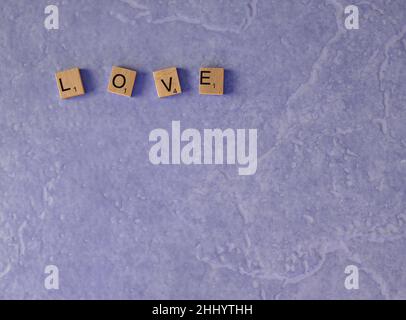 the word love spelt out in wooden squares on a light purple background shot from above copy space Stock Photo