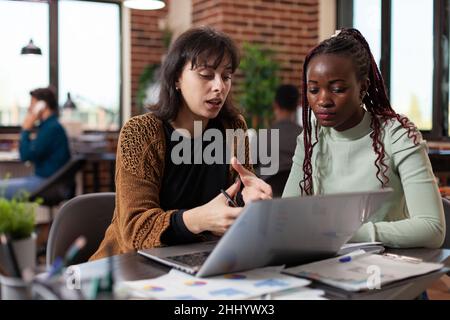 Multiracial businesswomen working at financial project analyzing marketing graphs on computer in startup office. Diverse team discussing company turnover planning business collaboration Stock Photo
