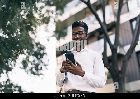 Smiling young black businessman using his smart phone in the city Stock Photo