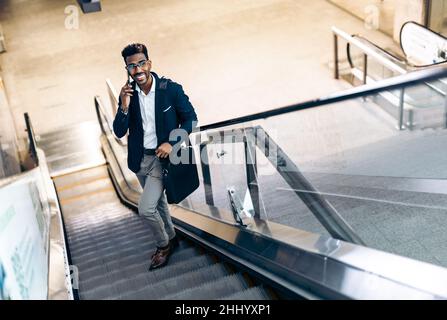 Smiling young black businessman using his smartphone on an escalator Stock Photo