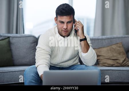 Press on and keep it productive. Shot of a young man using a laptop and smartphone while working from home. Stock Photo