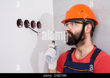 electrician in helmet installs sockets Stock Photo