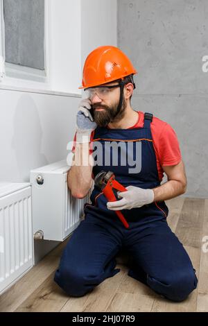 a worker in an orange helmet installs radiators in the house Stock Photo