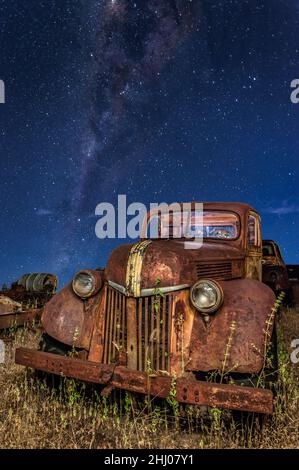 An old, abandoned, vintage ford pick-up lying in a grassy field on a Chillagoe property in Queensland with the milkyway core in the background. Stock Photo