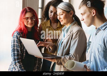 Mature teacher using laptop while talking with her students during class in art school indoors Stock Photo