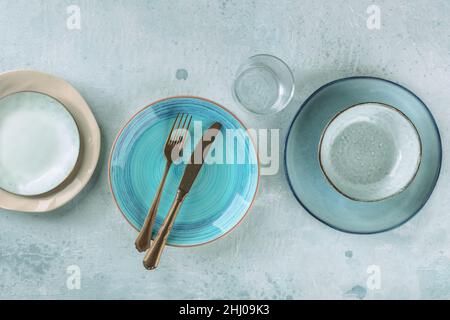 Modern dinnerware with cutlery. A vibrant blue plate with a fork and a knife, top shot with a glass and other tableware Stock Photo