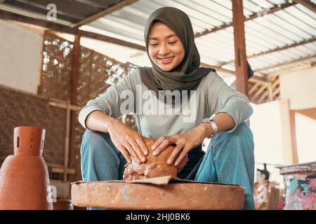woman in headscarf sitting relaxed holding wet clay on wheels Stock Photo