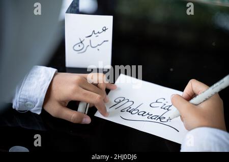 Child's hand writes a happy Eid Mubarak greeting card Stock Photo