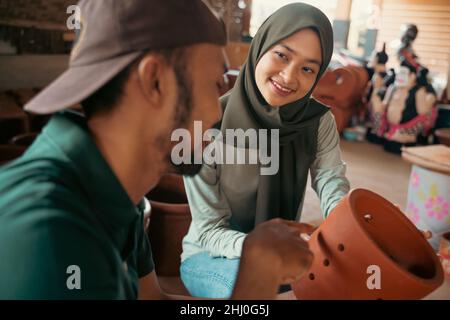 veiled woman observing pottery craft with young man Stock Photo