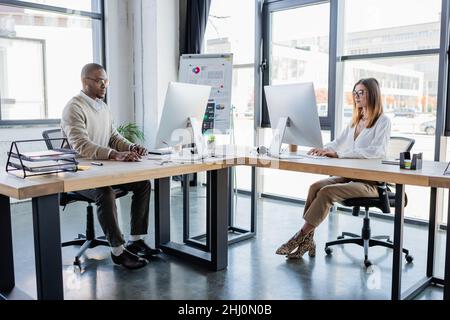 interracial colleagues in glasses looking at computer monitors while working in modern office Stock Photo