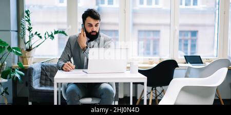 Thoughtful businessman taking notes talking on smartphone Stock Photo