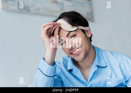 cheerful young man taking off sleep mask and looking at camera Stock Photo