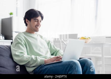 pleased man using laptop while sitting on couch at home Stock Photo