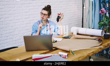 Concentrated tailor working at table with drawings and laptop Stock Photo
