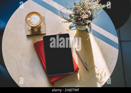Table with tablet located on planner and cup of cappuccino near flowers Stock Photo