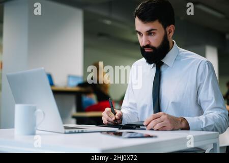 Focused businessman taking notes from laptop while working in modern workspace Stock Photo