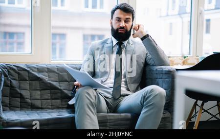 Tired businessman with documents talking on phone Stock Photo