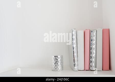 Stack of white and pink books staying on a shelf and white wall as background. copy space Stock Photo