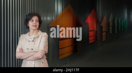 Pretty middle aged business woman in business suit, successful confidence close up portrait against dark wall with up arrows in perspective Stock Photo