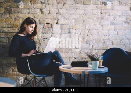 Young focused freelancer sitting with crossed legs and using laptop Stock Photo