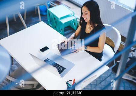 Smiling woman with notebook looking at laptop screen Stock Photo